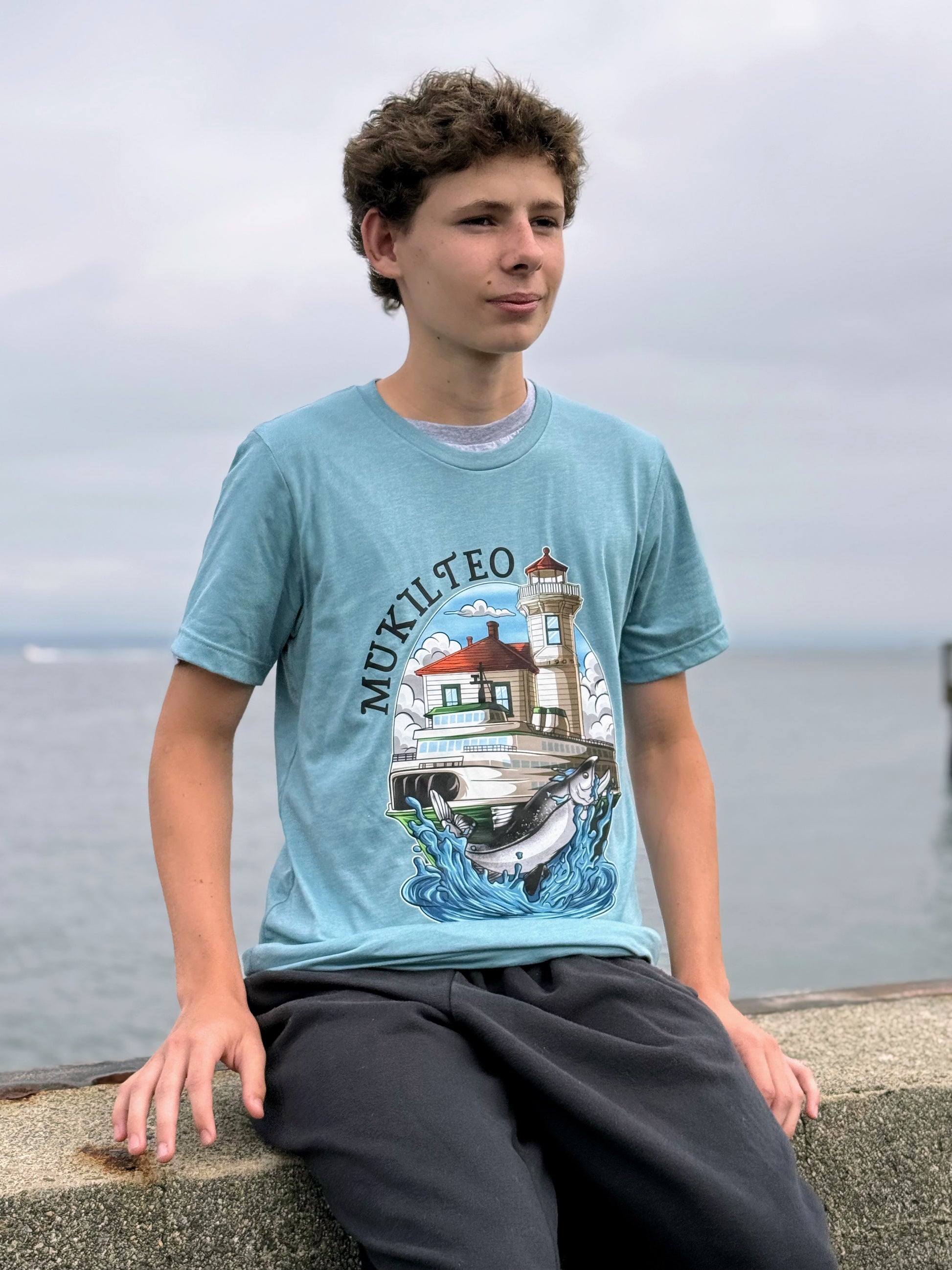Person wearing a light blue t-shirt with a lighthouse design, leaning.