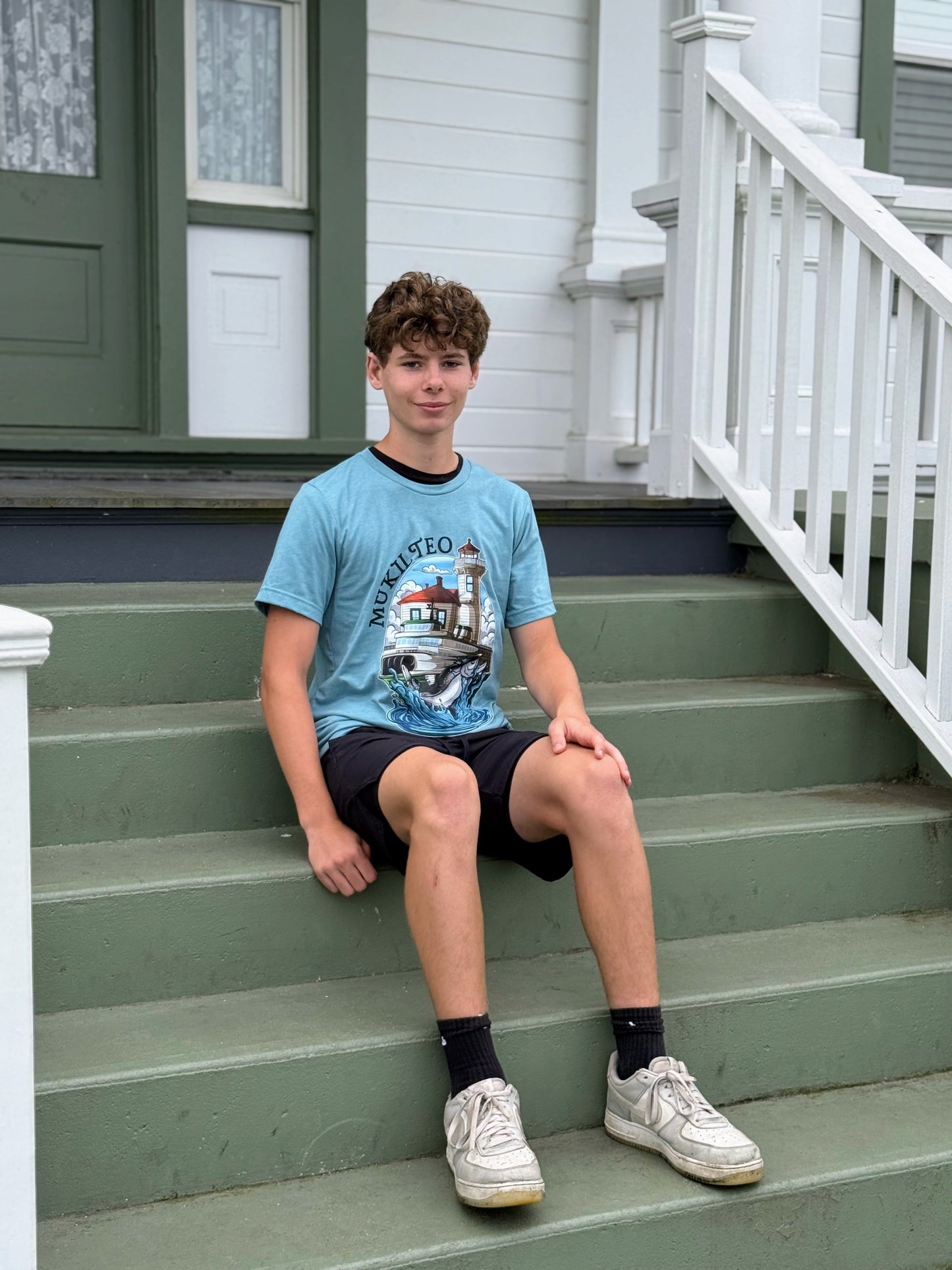 Young boy sitting on a green staircase wearing a light blue t-shirt with a graphic design.
