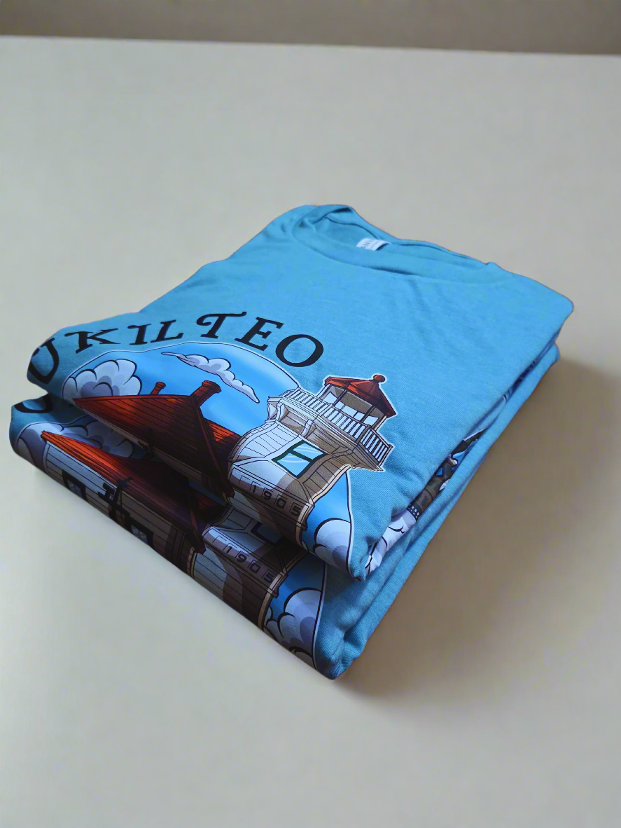 Folded blue t-shirt with a lighthouse design and 'Mukilteo' branding