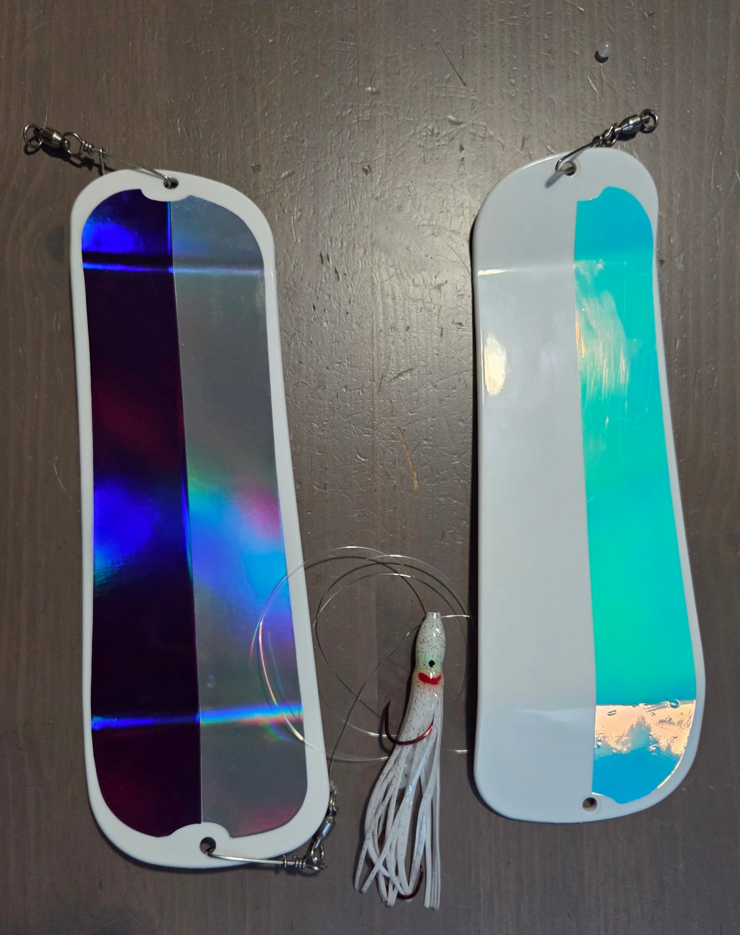 Two metallic fishing lures on a dark surface with a small fishing hook and line.