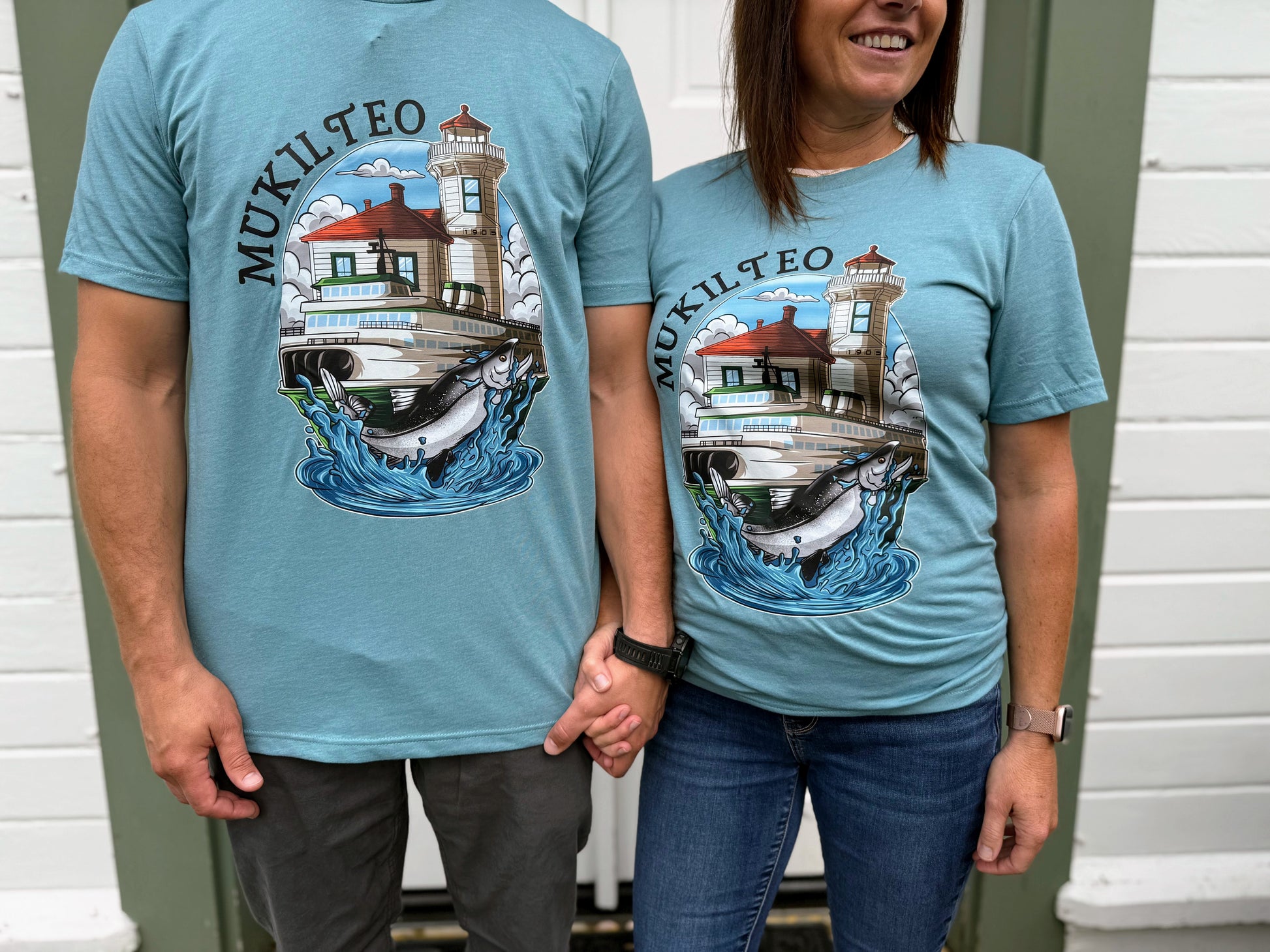 Two people wearing blue t-shirts with a lighthouse and salmon design, standing side by side.